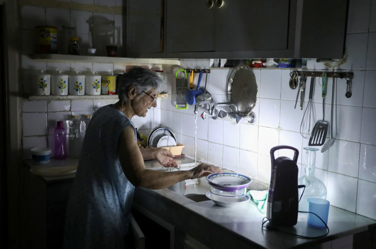 A woman washes dishes in her kitchen as she uses a portable electric light due to a power cut, in Beirut, Lebanon July 6, 2020. Picture taken July 6, 2020. Reuters
