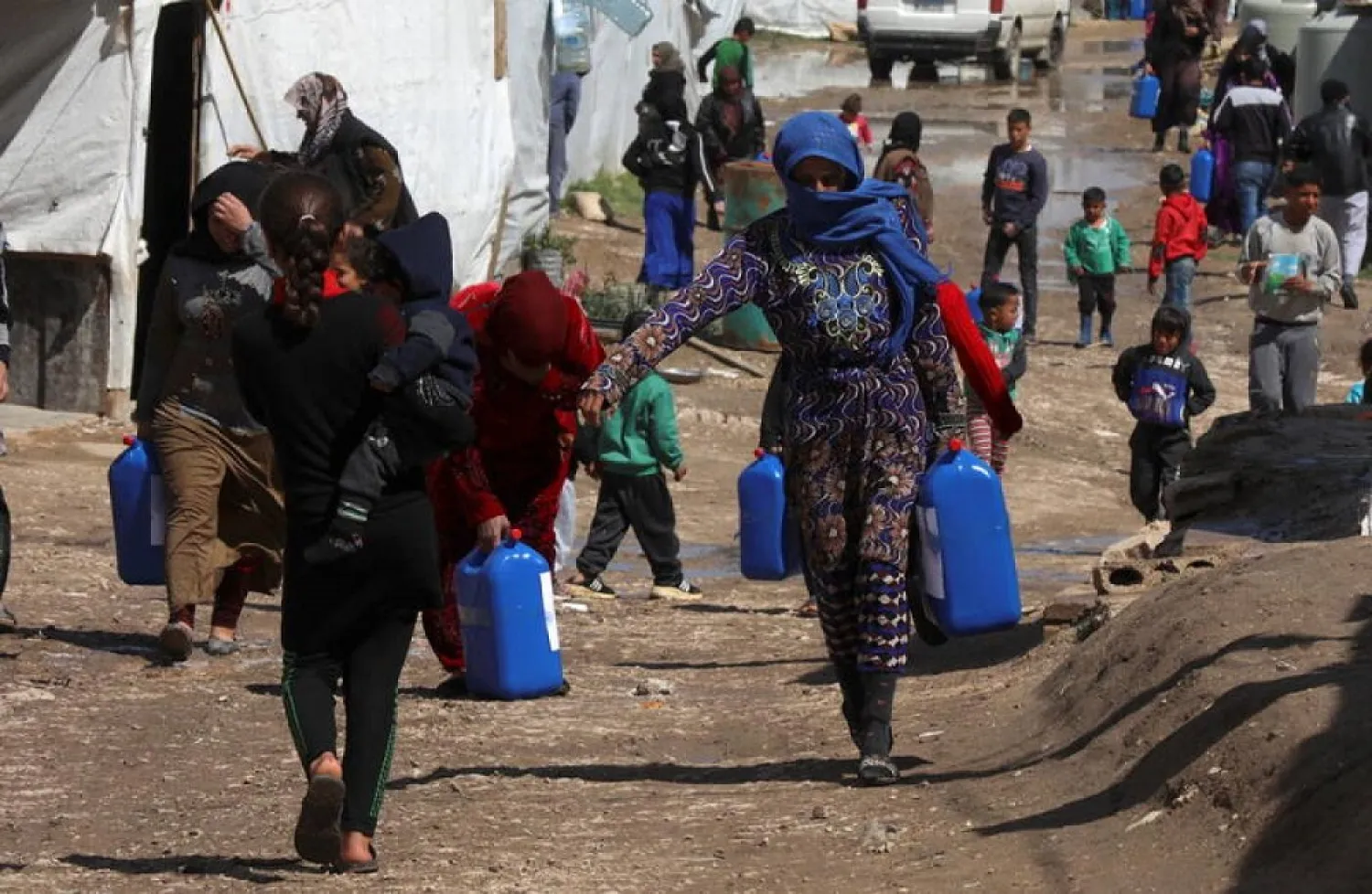 Syrian refugees walk as they carry containers at an informal tented settlement in the Bekaa valley, Lebanon March 12, 2021. (Reuters)