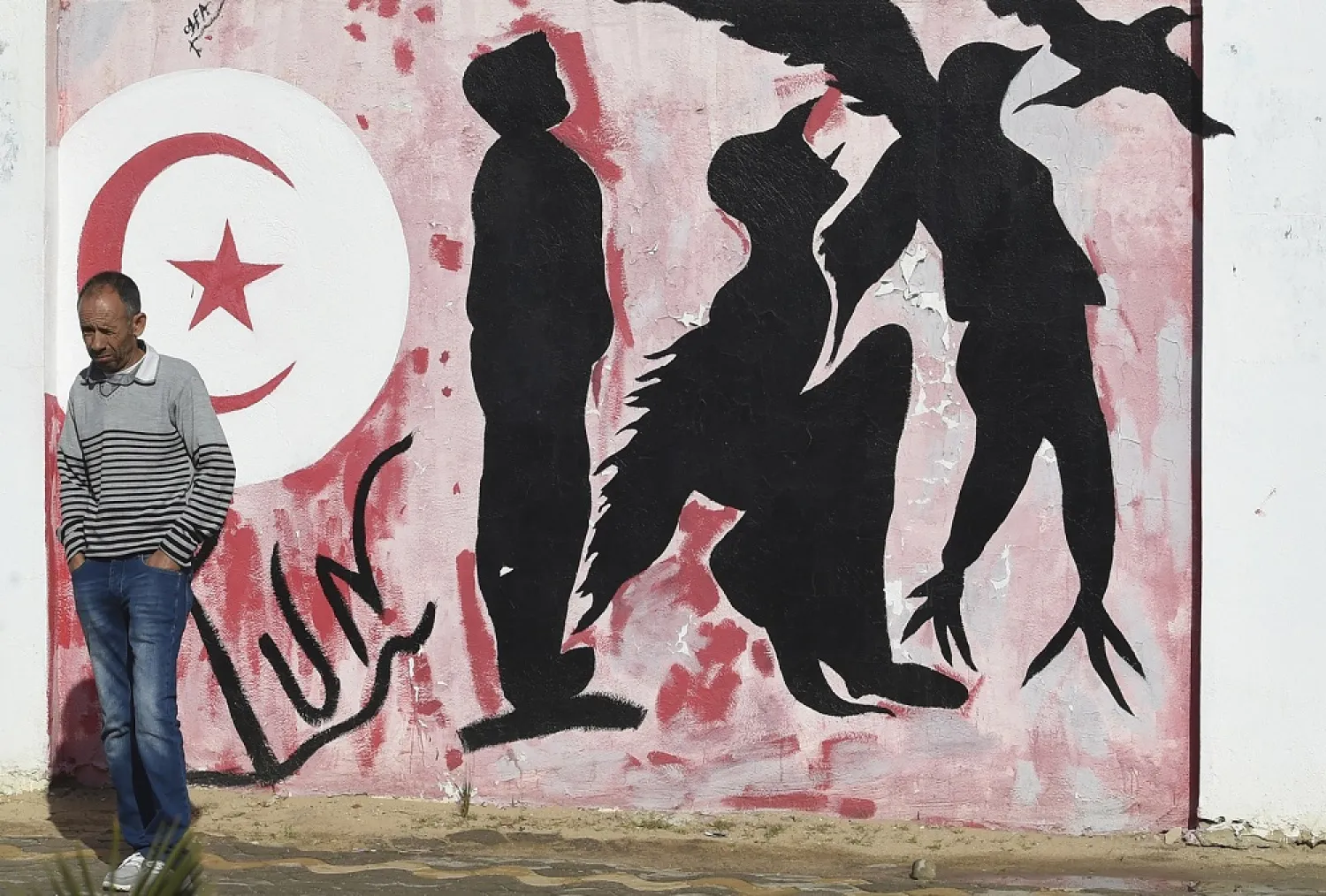 A man stands in front of graffiti in Mohamed Bouazizi Square in the town of Sidi Bouzid, cradle of the 2011 Tunisian revolution. (AFP)