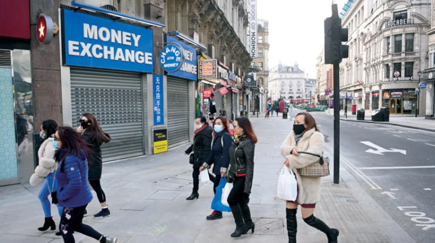 مجموعة من سكان لندن تمر أمام محلات مغلقة أمس في الذكرى الأولى لإعلان الحظر الصحي (إ.ب.أ)