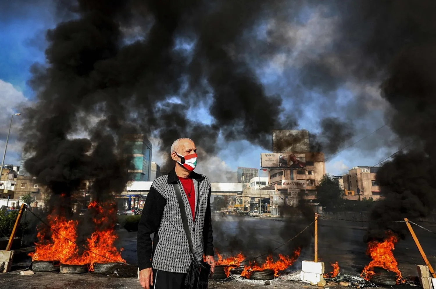 A man stands next to flaming tires at a makeshift roadblock set up by anti-government demonstrators in the area of Dora on the northern outskirts of Lebanon's capital Beirut on March 8, 2021. (AFP)