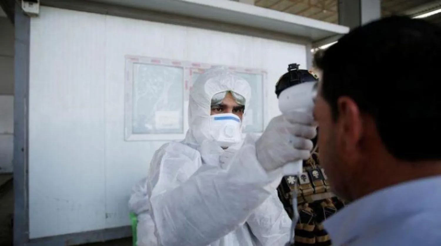 أحد أفراد طاقم طبي يفحص حرارة شخص في الموصل (رويترز)