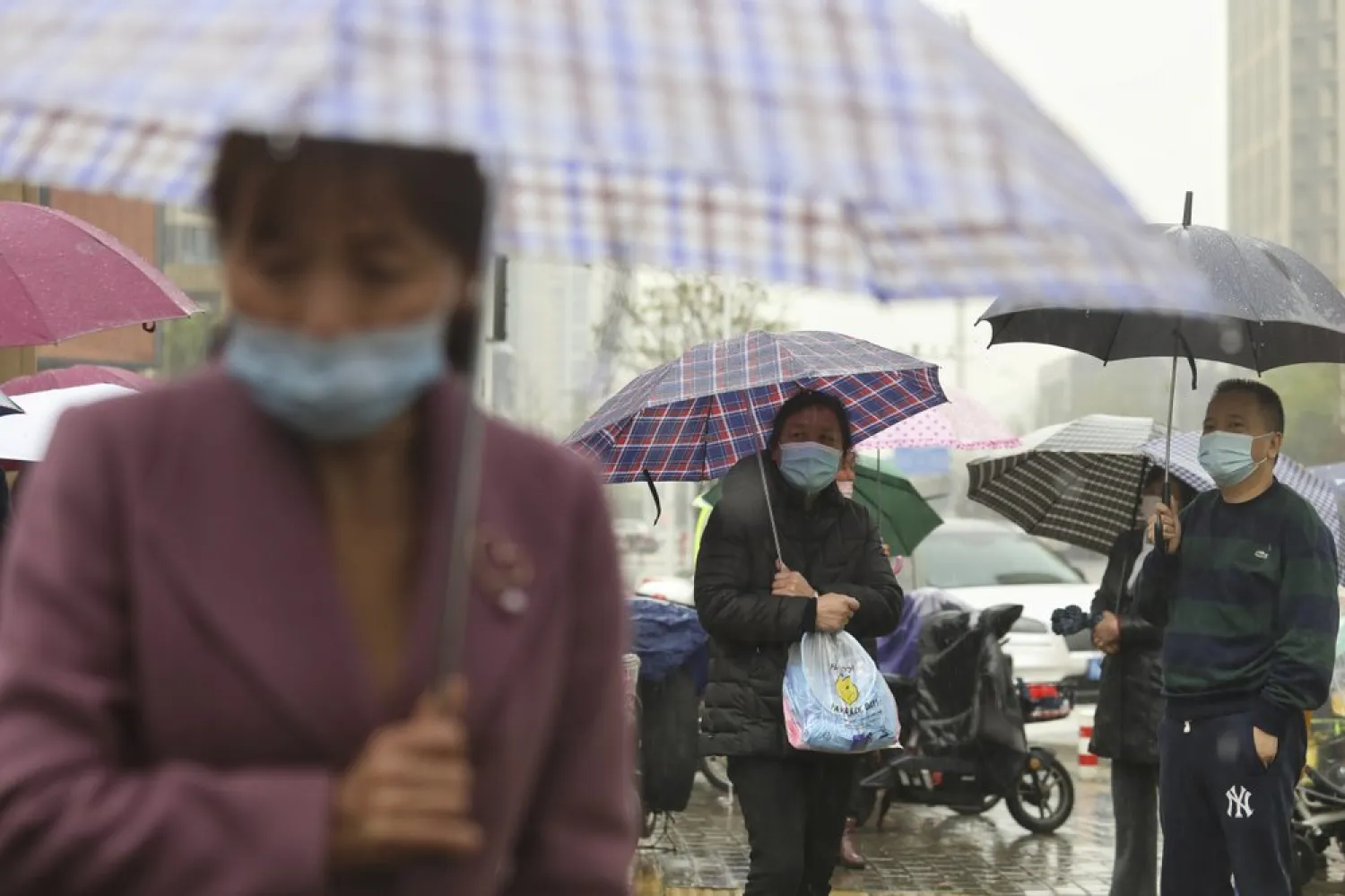 People wearing face masks to protect against COVID-19 wait in the rain to pick up children from a school in Wuhan in central China's Hubei Province, Friday, March 26, 2021. (AP)