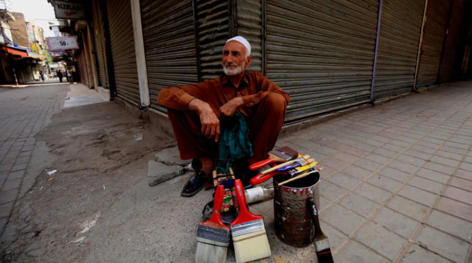 عامل أمام محل مغلق بعدما شددت باكستان القيود أمس (إ.ب.أ)