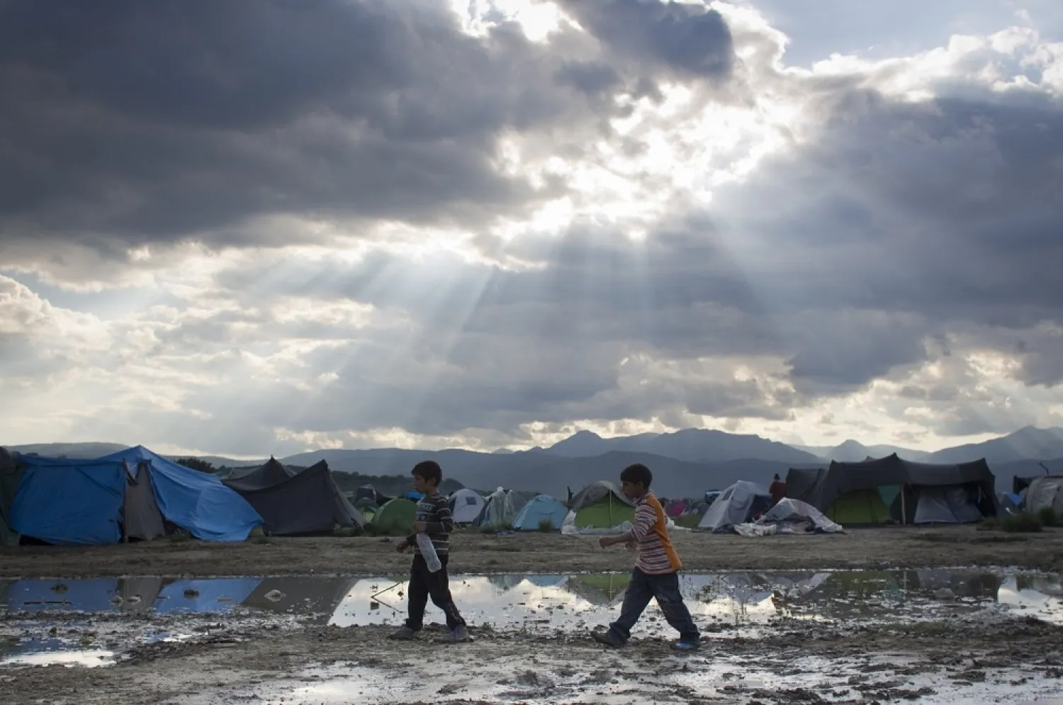 Two boys walk past groundwater at the migrant camp in Idomeni, northern Greece on May 22, 2016. (AP file photo)