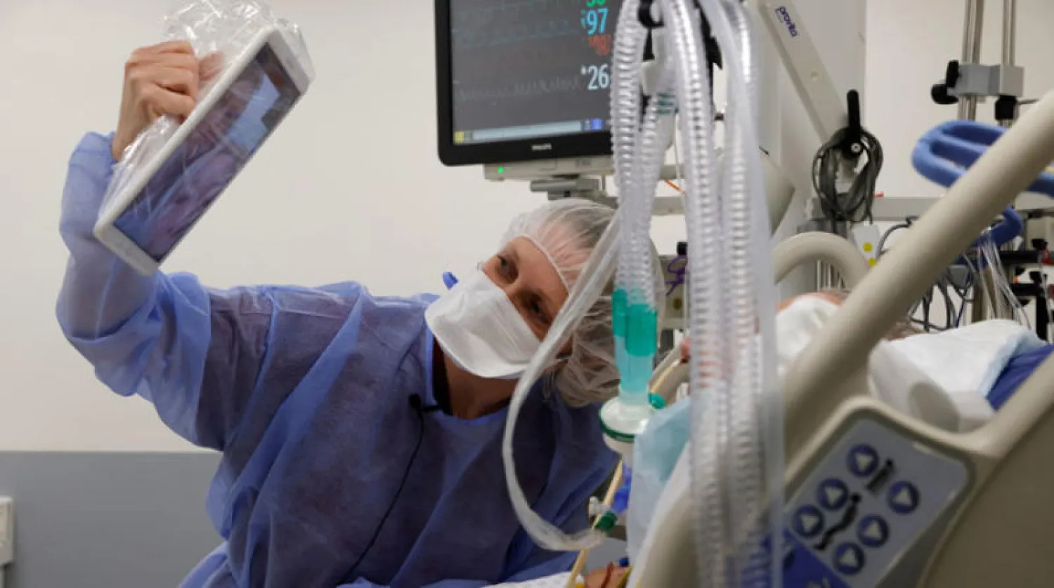 ممرضة تساعد مصاباً بـ«كوفيد - 19» على التواصل مع أسرته افتراضياً في مستشفى قرب باريس أمس (رويترز)