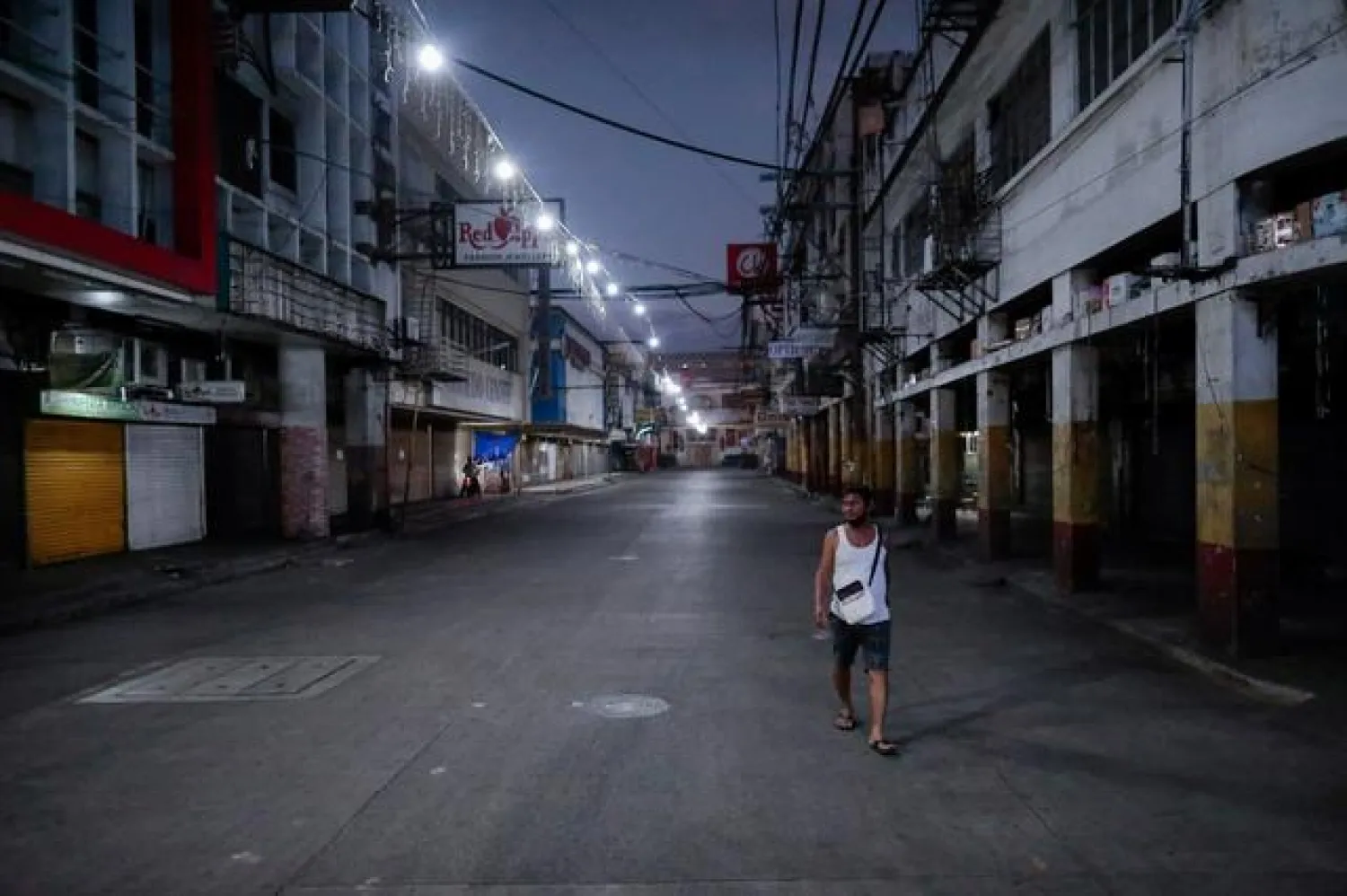 FILE PHOTO: A man wearing a protective mask on his neck walks past closed shops in an empty street following the lockdown in the Philippine capital to prevent the spread of the coronavirus disease (COVID-19), in Manila, Philippines, March 24, 2020. REUTERS/Eloisa Lopez 
