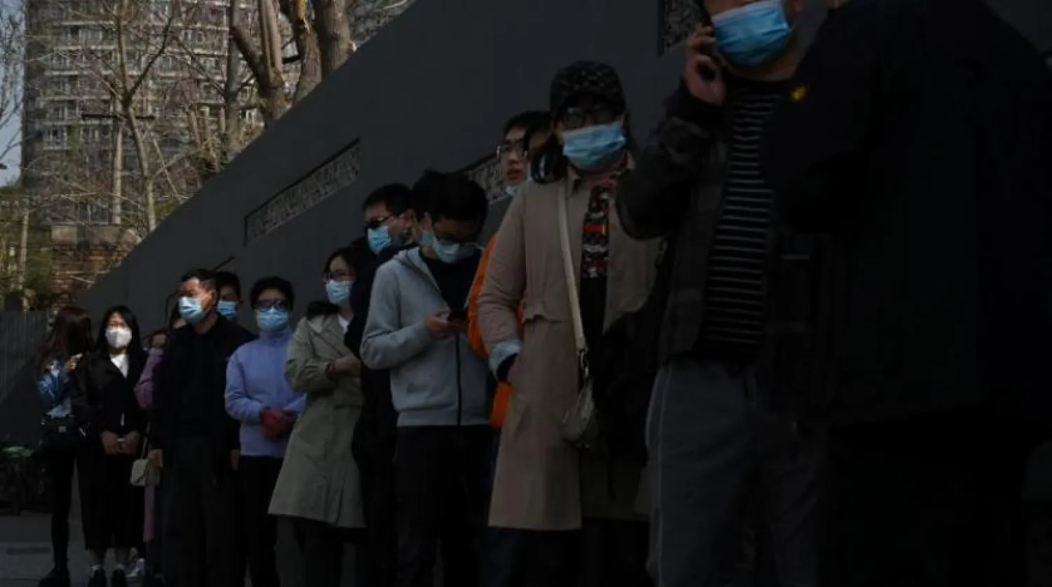 İnsanlar Pekin'de Kovid-19'a karşı aşı olmak için bir merkezin önünde maske takıyorlar (AFP)
