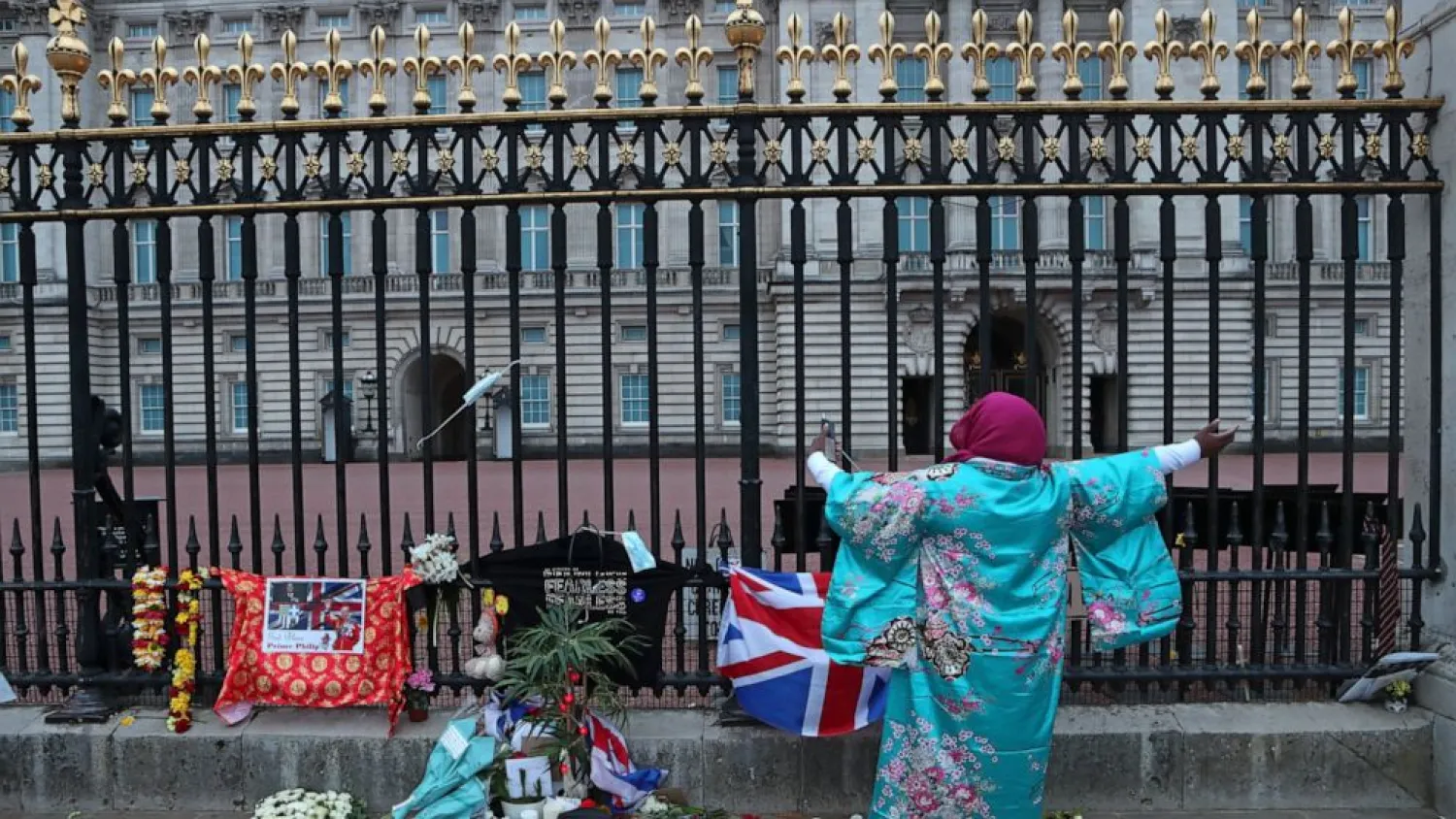 A woman gestures as she sings next to tributes left in honor of Britain's Prince Philip in front of Buckingham Palace in London on Saturday, April 10, 2021. Prince Philip, the irascible and tough-minded husband of Queen Elizabeth II who spent more than seven decades supporting his wife in a role that both defined and constricted his life, has died, Buckingham Palace said Friday. He was 99. (AP Photo/Tony Hicks)