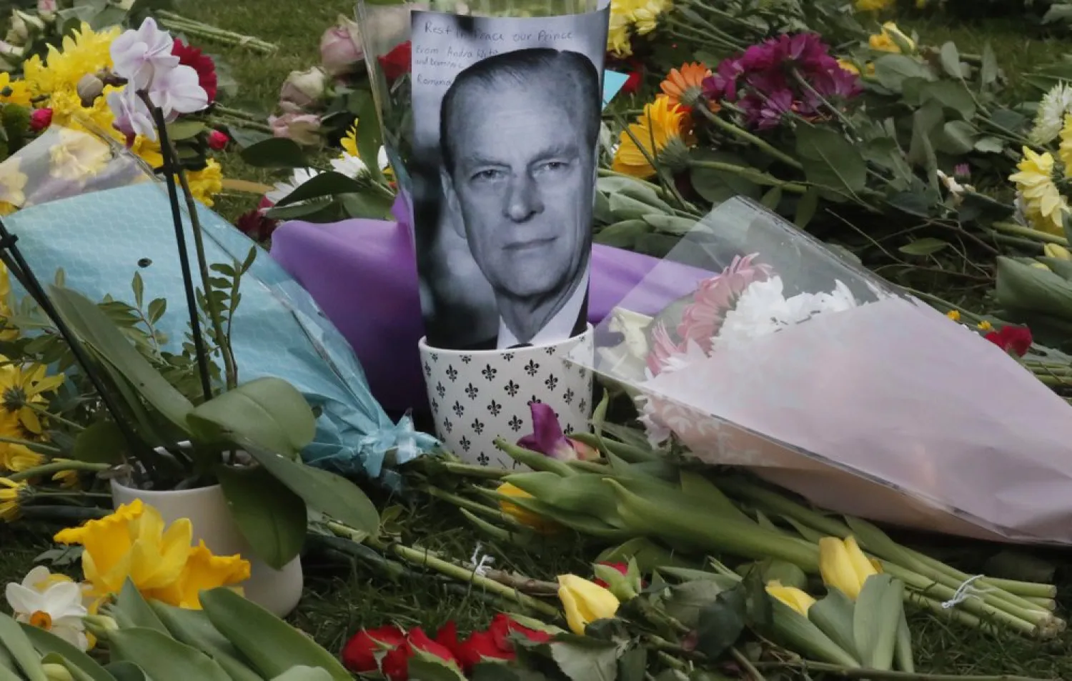 A photo of Britain's Prince Philip is among flowers left by the public outside the gates of Windsor Castle, a day after the death of Britain's Prince Philip, in Windsor, England, Saturday, April 10, 2021. (AP)