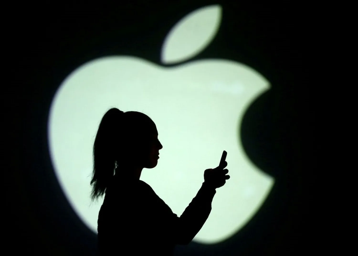 Silhouette of a mobile user seen next to a screen projection of the Apple logo in this picture illustration taken March 28, 2018. (Reuters)