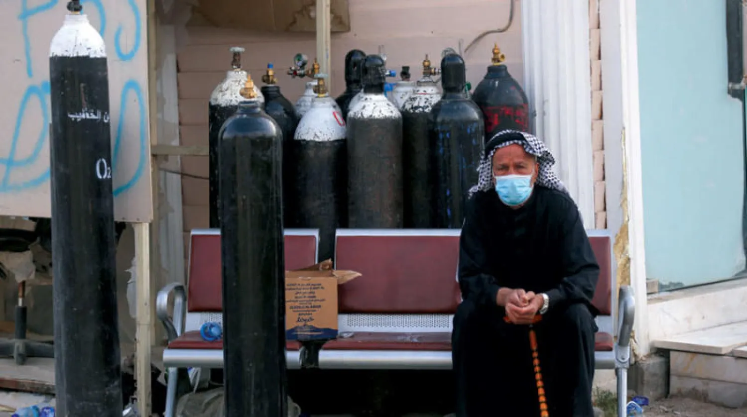 زوج مصابة بـ«كورونا» يجلس محاطاً بإسطوانات أكسجين في انتظار زيارتها بـ«مستشفى ابن الخطيب» ببغداد أمس (أ.ف.ب)