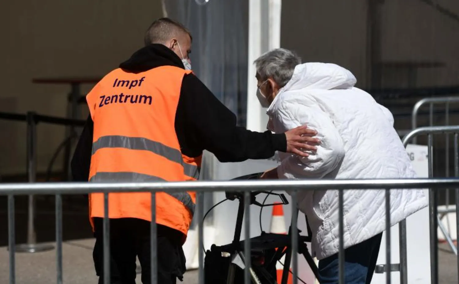 أحد أعضاء مركز التطعيم يساعد رجلاً عند مدخل مركز التطعيم في دويسبورغ غرب ألمانيا (أ.ف.ب)