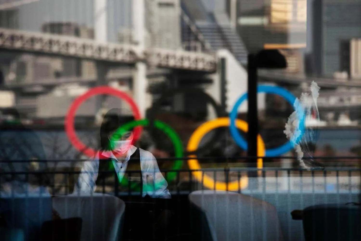 In this Feb. 24, 2020, photo, the Olympics rings are reflected on the window of a hotel restaurant as a server with a mask sets up a table, in the Odaiba section of Tokyo. (AP Photo/Jae C. Hong, File)