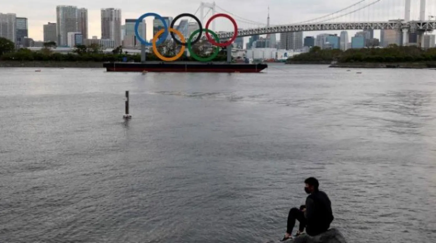 رجل يجلس على صخرة بالقرب من الشعار الأولمبي في طوكيو (أ.ف.ب)