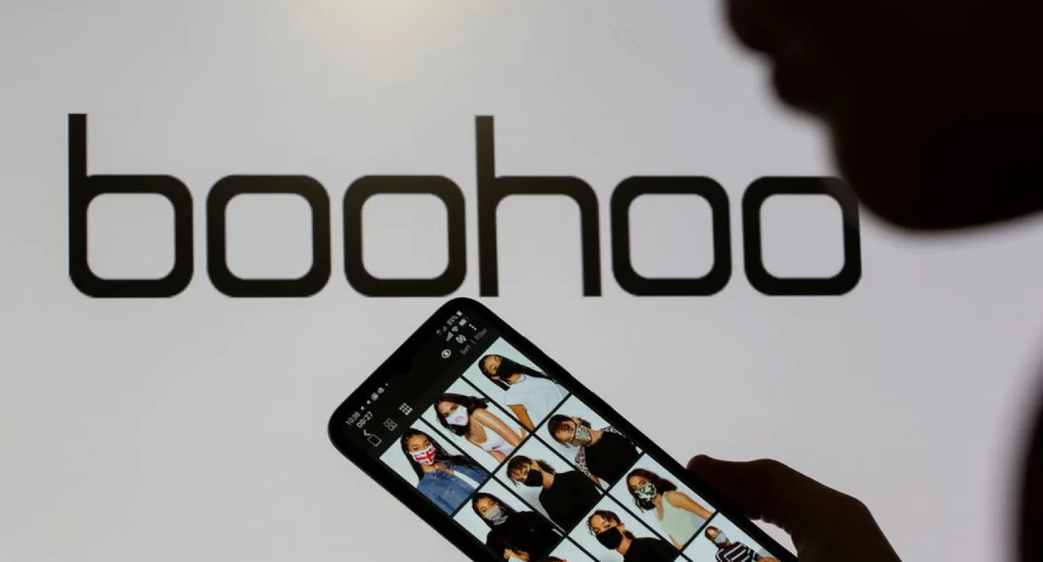A woman poses with a smartphone showing the Boohoo app in front of the Boohoo logo on display in this illustration taken September 30, 2020. REUTERS/Dado Ruvic/Illustration/File Photo

