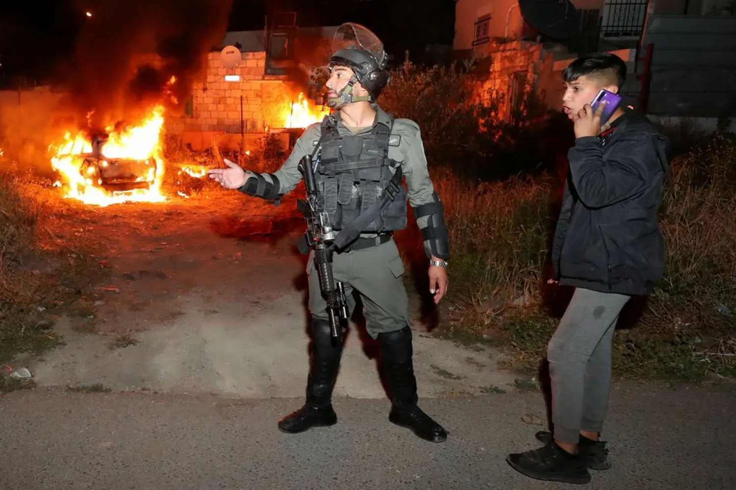 An Israeli policeman gestures as a car belonging to Jewish settlers burns amid tension over the possible eviction of several Palestinian families from homes on land claimed by Jewish settlers in the Sheikh Jarrah neighbourhood in East Jerusalem, May 6, 2021. REUTERS/Ammar Awad

