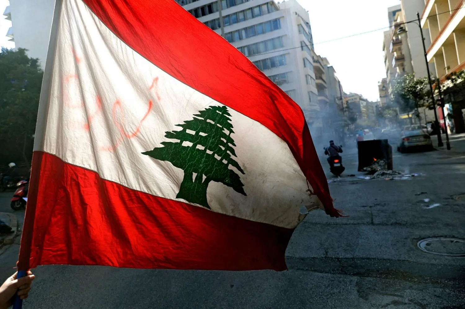 An anti-government demonstrator waves the national flag as they block the street, with burning garbage dumpsters, in front of Lebanon’s central bank in the capital Beirut on March 16, 2021. (AFP)