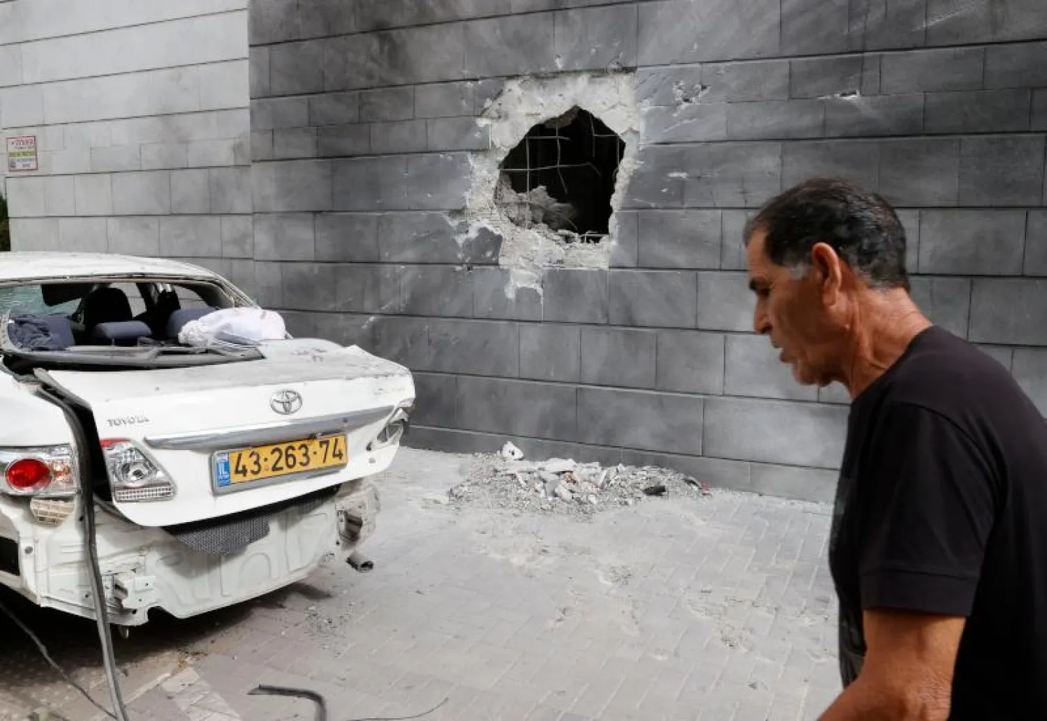 رجل إسرائيلي يسير بجانب جدار مثقوب جراء أحد صواريخ حركة "حماس" في مدينة عسقلان (أ.ف.ب)