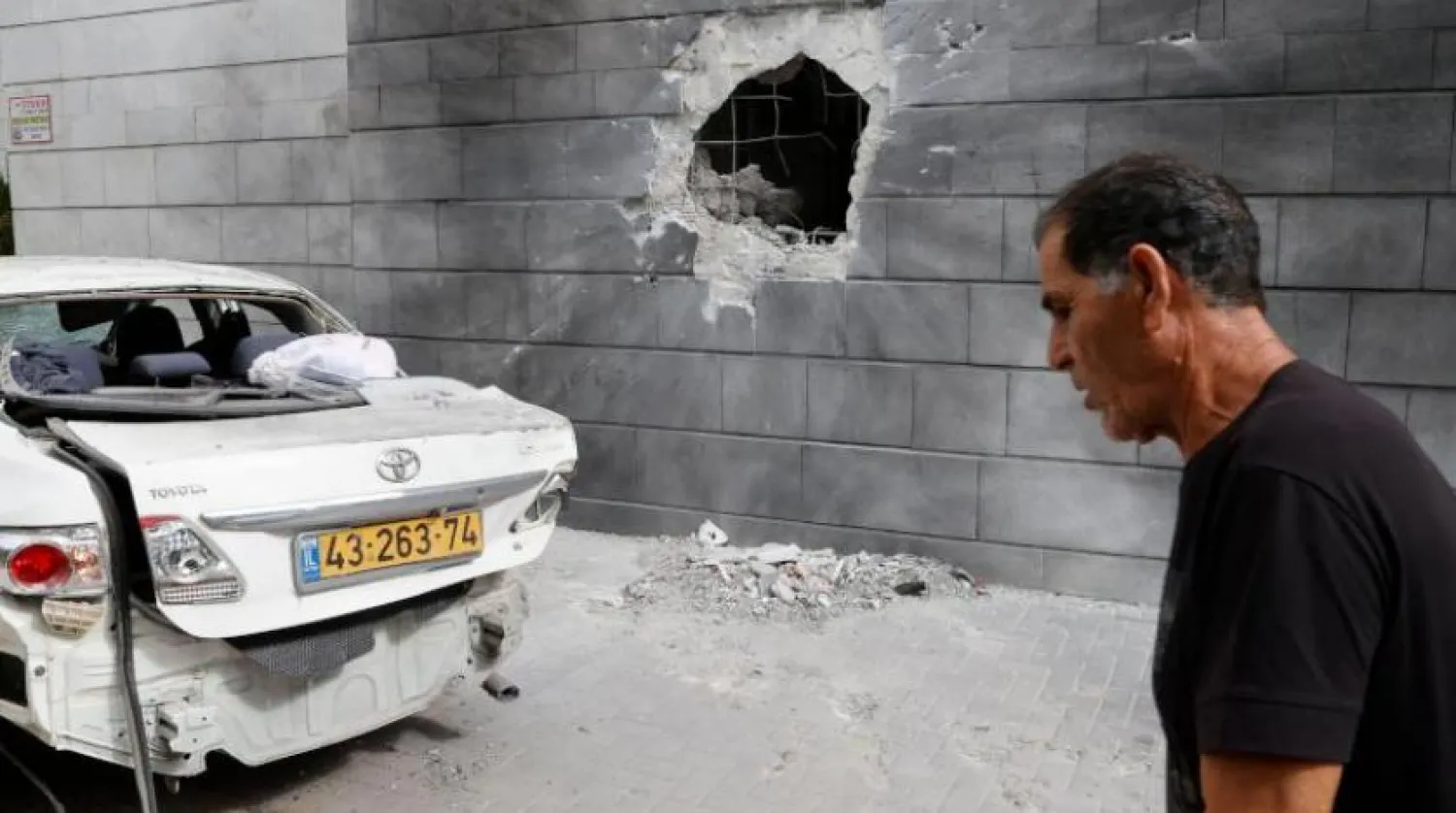 İsrailli bir adam, Aşkelon'da Hamas tarafından atılan bir roketin isabet ettiği duvarın yanında yürüyor (AFP) 
