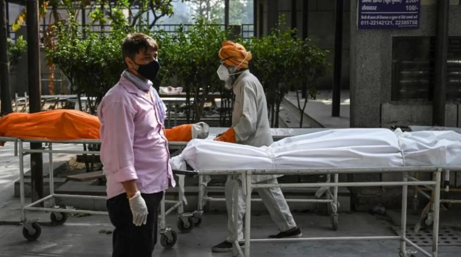 Yeni Delhi'de korona kurbanlarının cesetlerinin yanında iki gönüllü duruyor (AFP)
