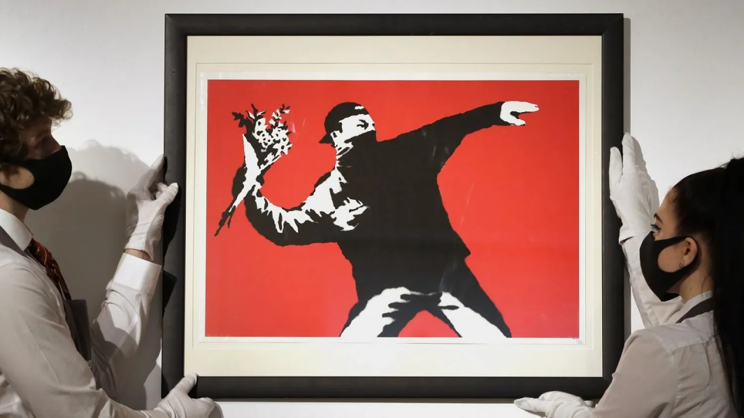 Gallery technicians display a Banksy artwork called "Love is in the Air" read for auction.   -   Copyright  Kirsty Wigglesworth/Associated Press
