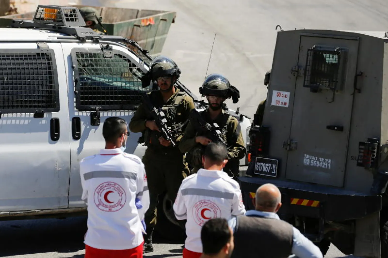 مسعفون فلسطينيون يقفون أمام عناصر من القوات الإسرائيلية في موقع حادث أمني في الخليل بالضفة الغربية المحتلة (رويترز)