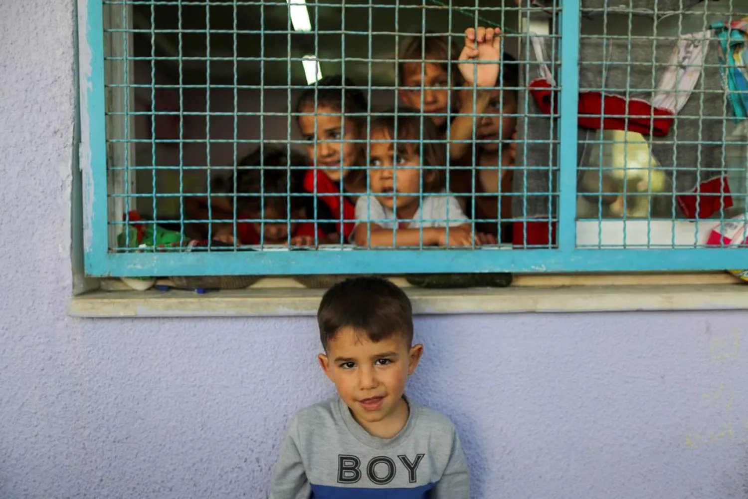 A Palestinian boy, who fled his family's home due to Israeli air and artillery strikes, looks on as other children look through a window fence at a United Nations-run school where they take refuge, in Gaza City May 18, 2021. REUTERS/Suhaib Salem

