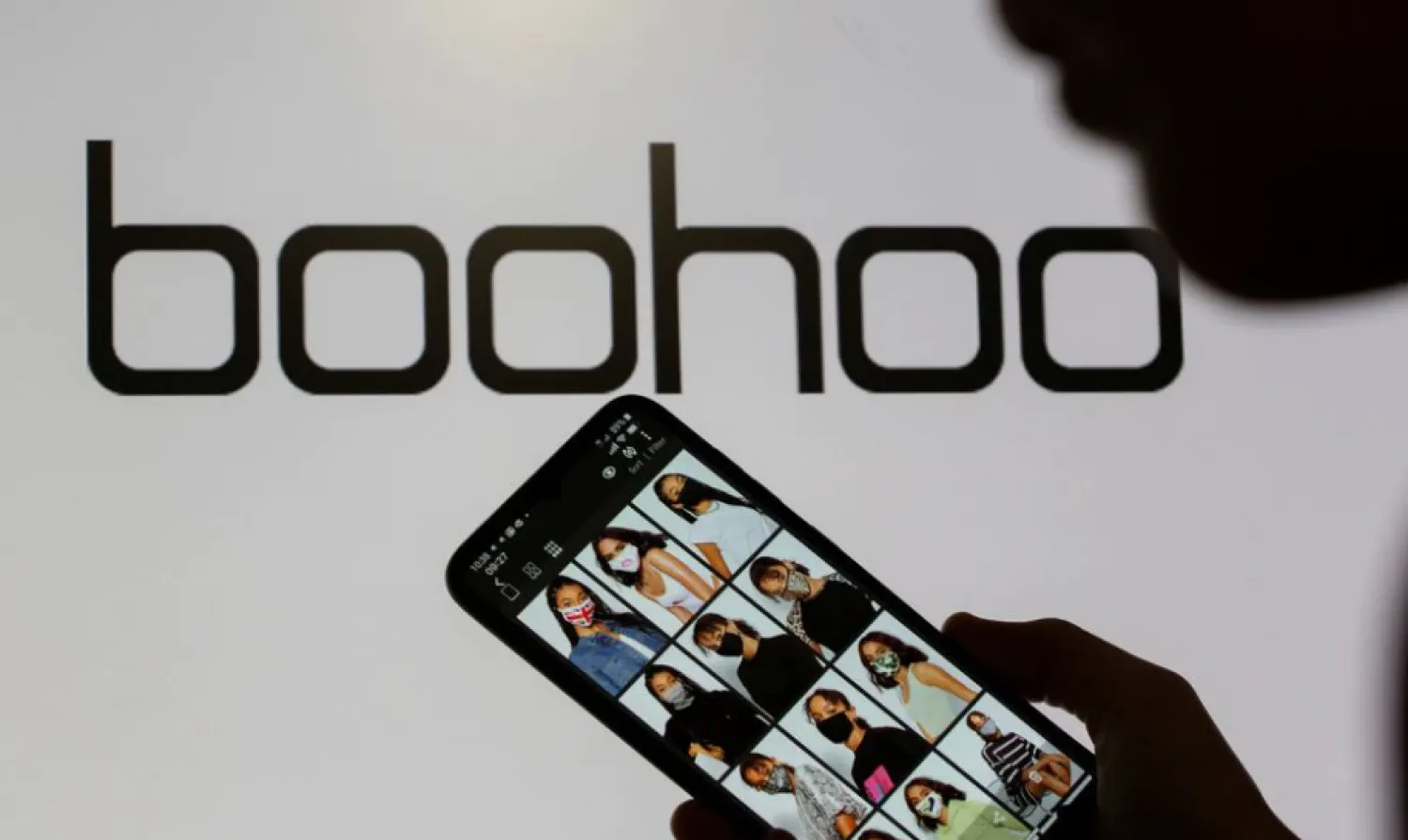 A woman poses with a smartphone showing the Boohoo app in front of the Boohoo logo on display in this illustration taken September 30, 2020. REUTERS/Dado Ruvic/Illustration



