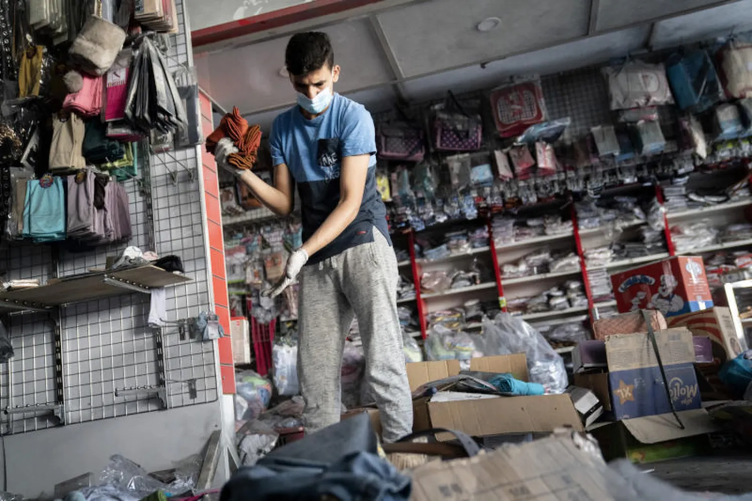 موظف يرتدي القناع الواقي بينما يحاول إزالة ما تبقى من سلع داخل احد المتاجر المتضررة في قطاع غزة (أ.ب)
