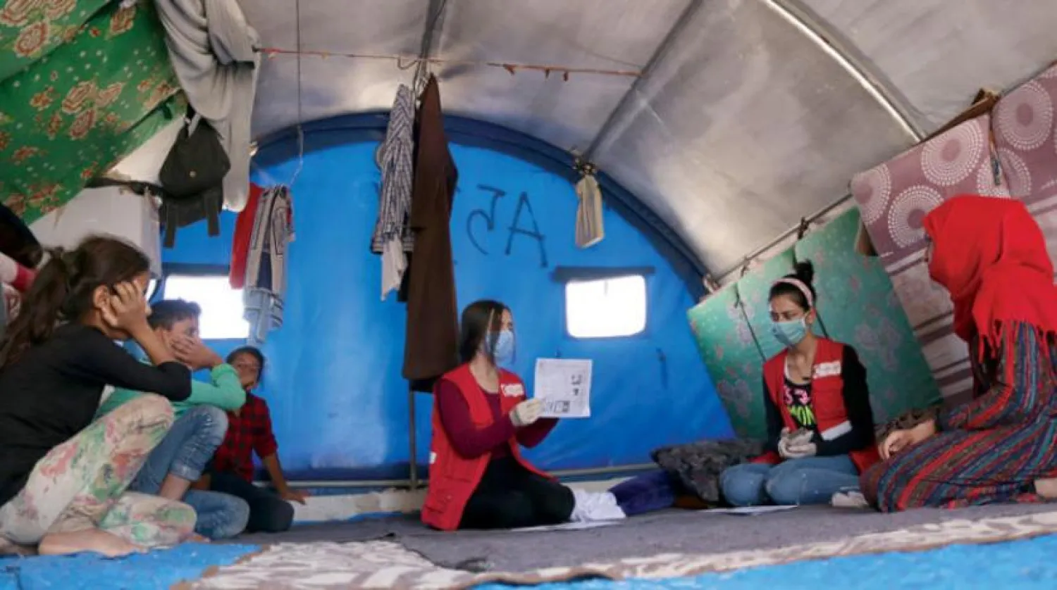 A volunteer distributes pamphlets raising awareness about the COVID-19 at a displacement camp in Hasakah. (Asharq Al-Awsat)