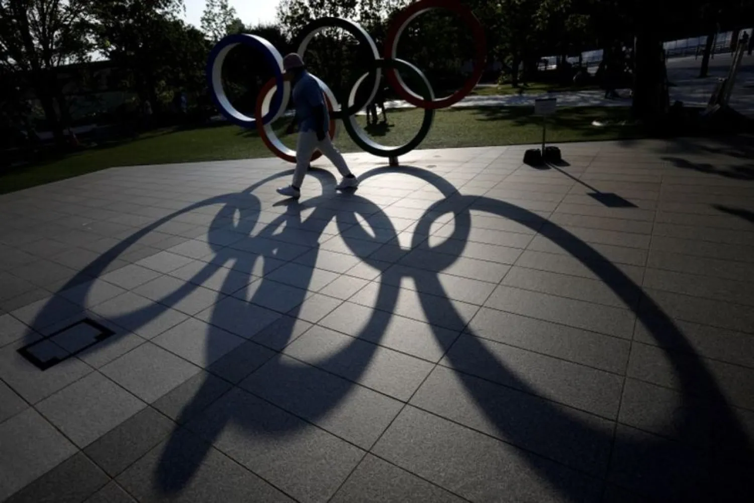 A visitor and the Olympic Rings monument cast shadows on the ground outside the Japan Olympic Committee (JOC) headquarters near the National Stadium, in Tokyo, Japan May 30, 2021. (Reuters)