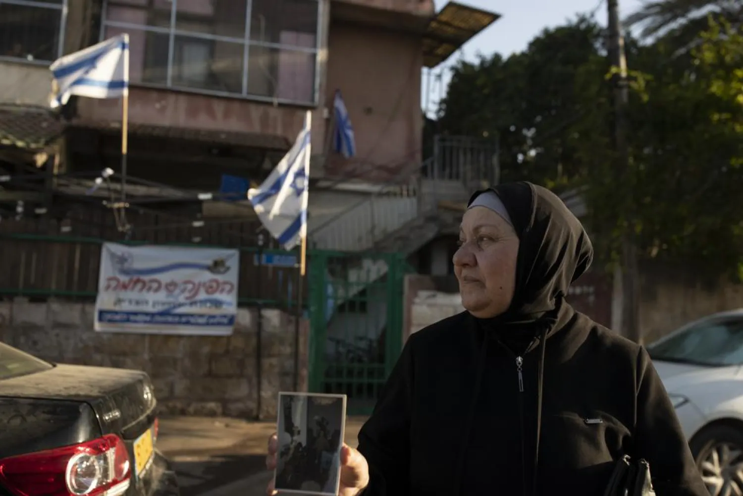 Maryam Ghawi, a Palestinian, holds a family photo taken in the home behind her that is now occupied by Israeli settlers in the Sheikh Jarrah neighborhood of east Jerusalem, May 25, 2021. (AP)