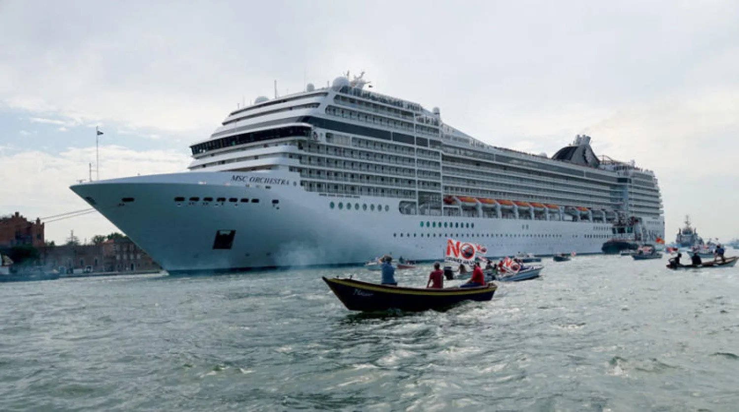 متظاهرون يلوّحون بلافتات اعتراضاً على إبحار السفينة «إم إس سي أوركسترا» في مياه البندقية (إ.ب.أ)