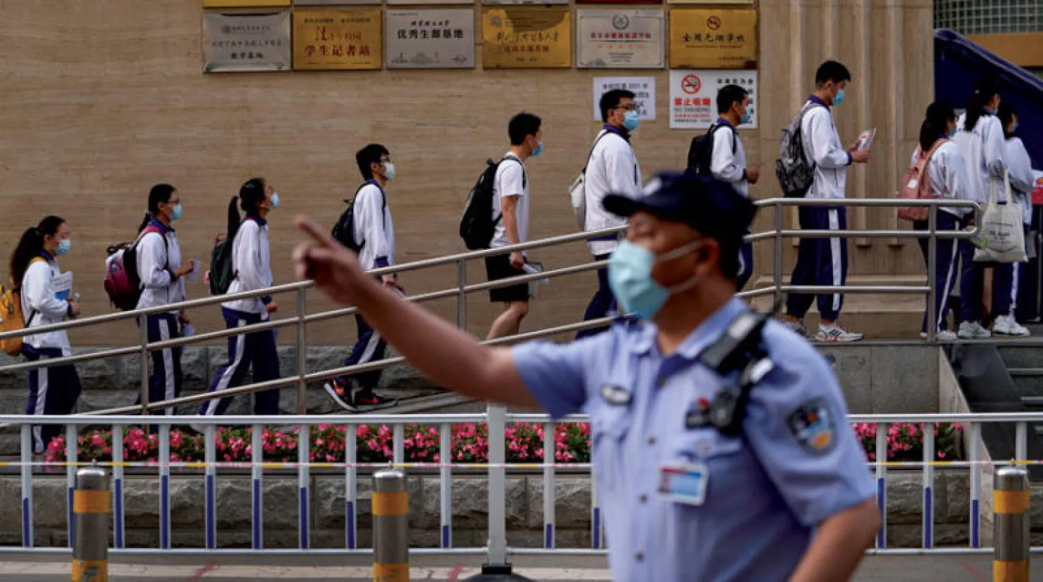 شرطي صيني يراقب دخول الطلاب إلى مدرسة في أول يوم من الاختبارات ببكين أمس وسط إجراءات صحية احترازية (أ.ب)