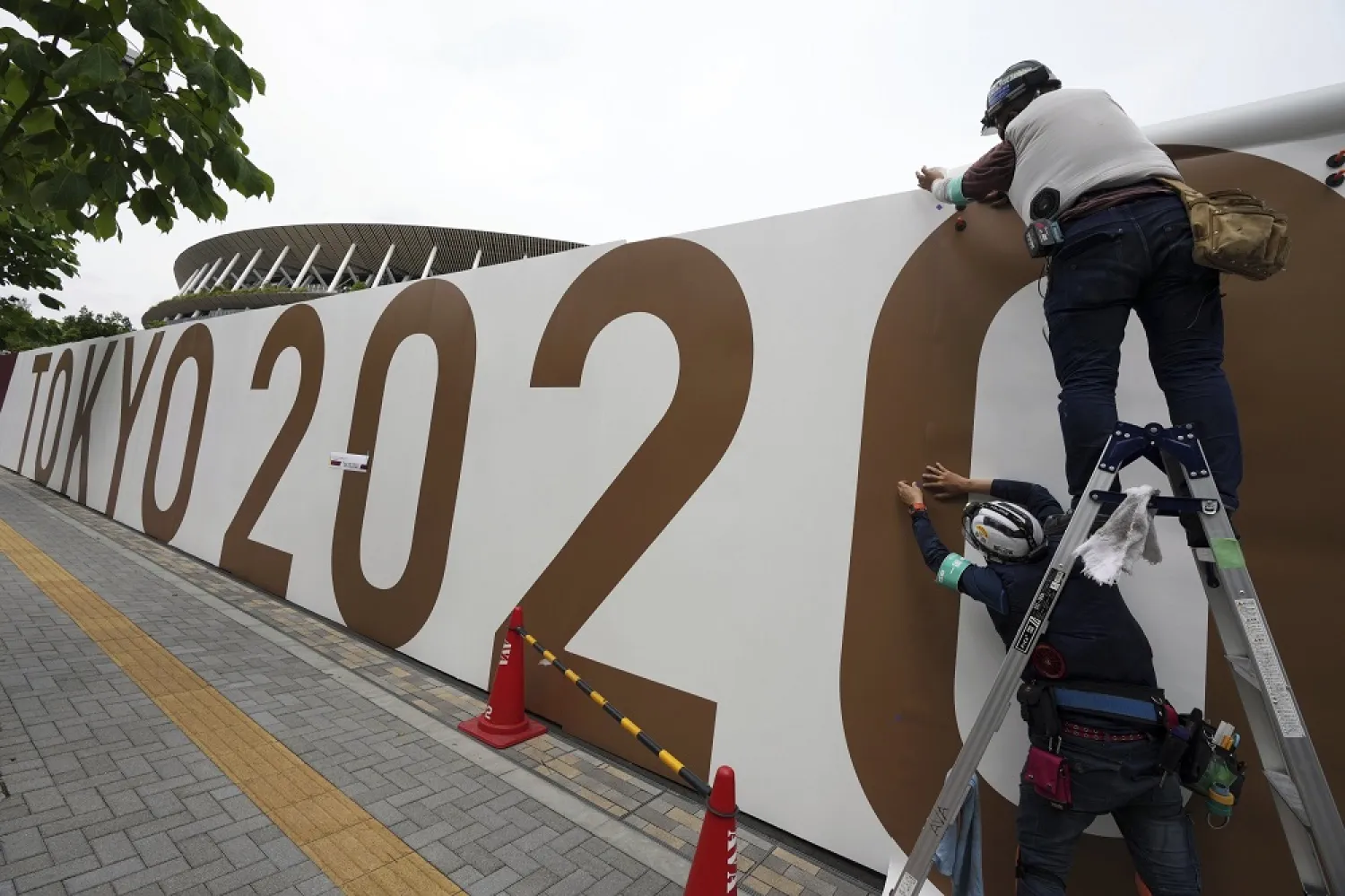 Workers paste the overlay on the wall of the National Stadium, where the opening ceremony and many other events are scheduled for the Tokyo 2020 Olympics, Tokyo, Japan, June 2, 2021. (AP)