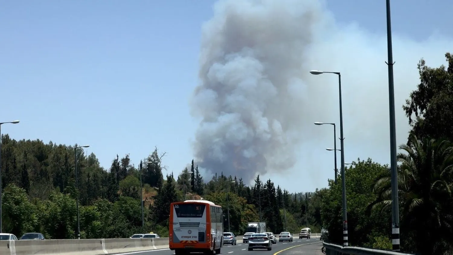 Cars drive on a highway as smoke billows from a forest fire in the area of the Arab-Israeli village of Abu Ghosh near Jerusalem, on June 9, 2021. (Emmanuel Dunand/AFP)
