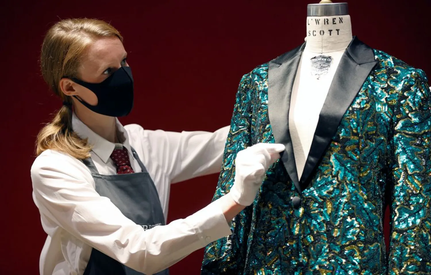 A gallery assistant poses for a photograph next to the Oak Leaf “Glamouflage” jacket designed for Mick Jagger by designer L’Wren Scott at Christie’s in London, Britain, June 10, 2021. (Reuters)