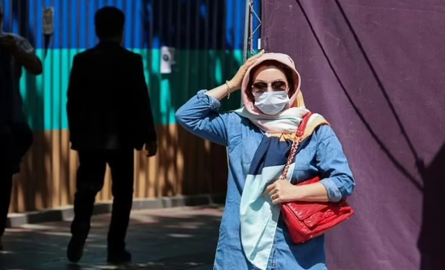 An Iranian woman wearing a protective mask adjusts her head scarf as she walks on a street in Tehran on April 12, 2021 - AFP