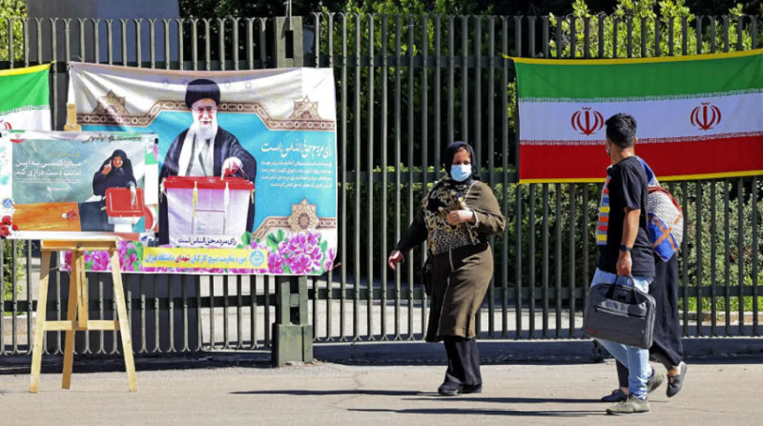 إيرانيون يمرون أمام لافتات تشجع على المشاركة في الانتخابات معلقة على سور جامعة طهران وسط العاصمة الإيرانية أمس (أ.ف.ب)