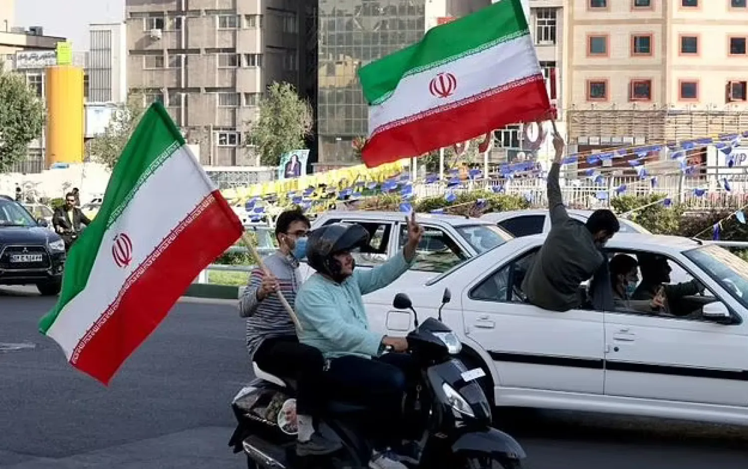 Iranians waving national flags drive past an electoral banner showcasing Iran's ultraconservative candidate Ebrahim Raisi during a street rally in the capital Tehran on June 15, 2021 - AFP