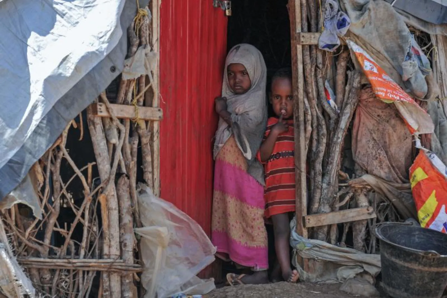 طفلتان صوماليتان تقفان عند مدخل مأوى مؤقت في مخيم للنازحين (أ.ف.ب)