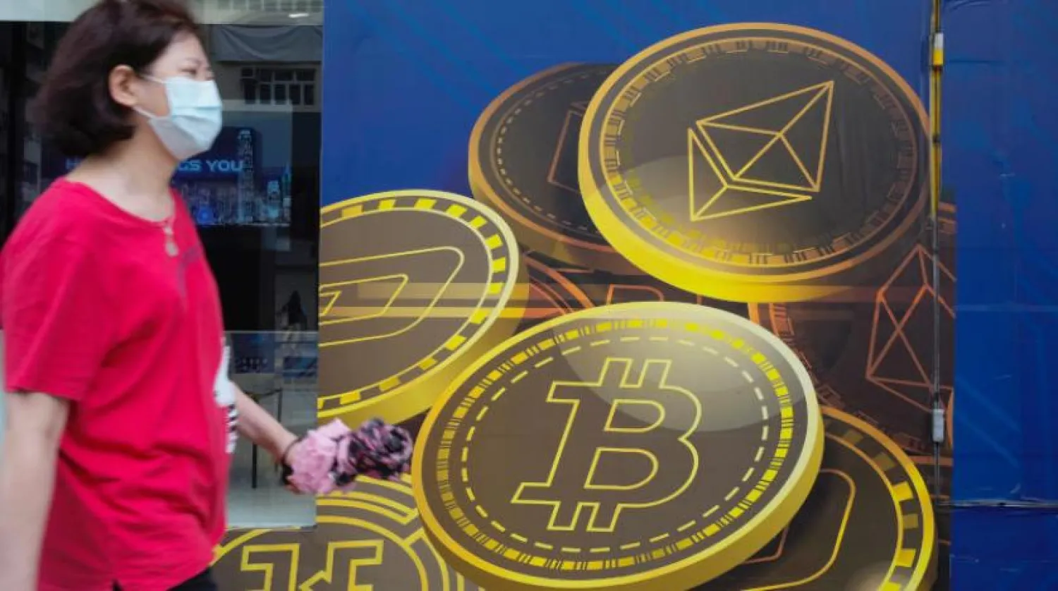 Hong Kong’da Bitcoin logosu taşıyan bir reklam panosunun yanından geçen bir kadın (AP)