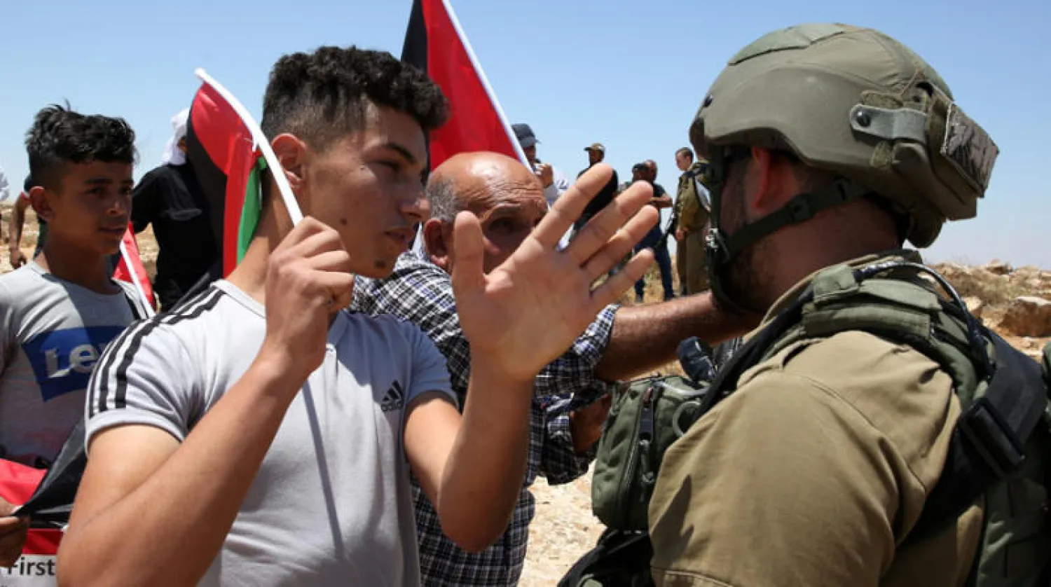 متظاهر فلسطيني يتجادل مع عنصر من قوات الأمن الإسرائيلية أثناء احتجاجات قرب الخليل أمس (إ.ب.أ)