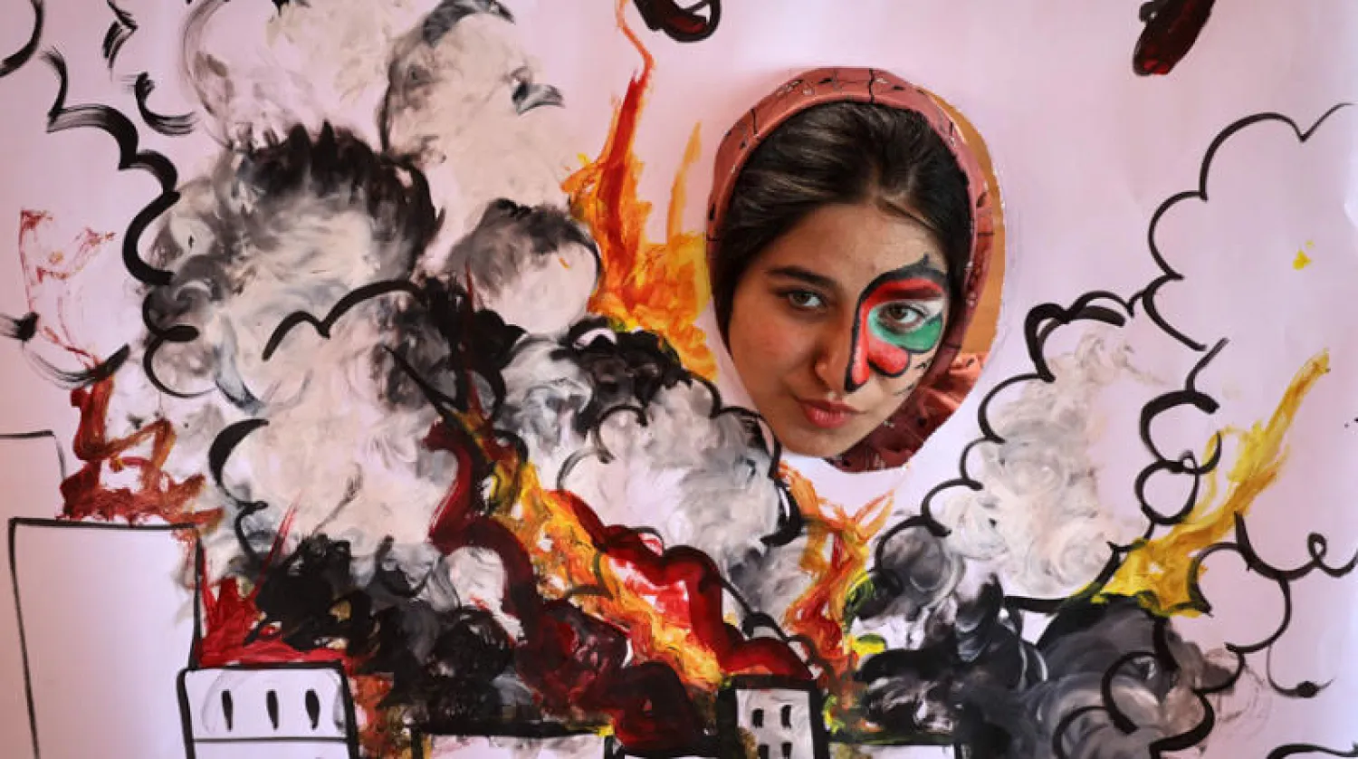 طفلة تطل من فتحة لوحة أعدها أطفال فلسطينيون في غزة (أ.ف.ب)