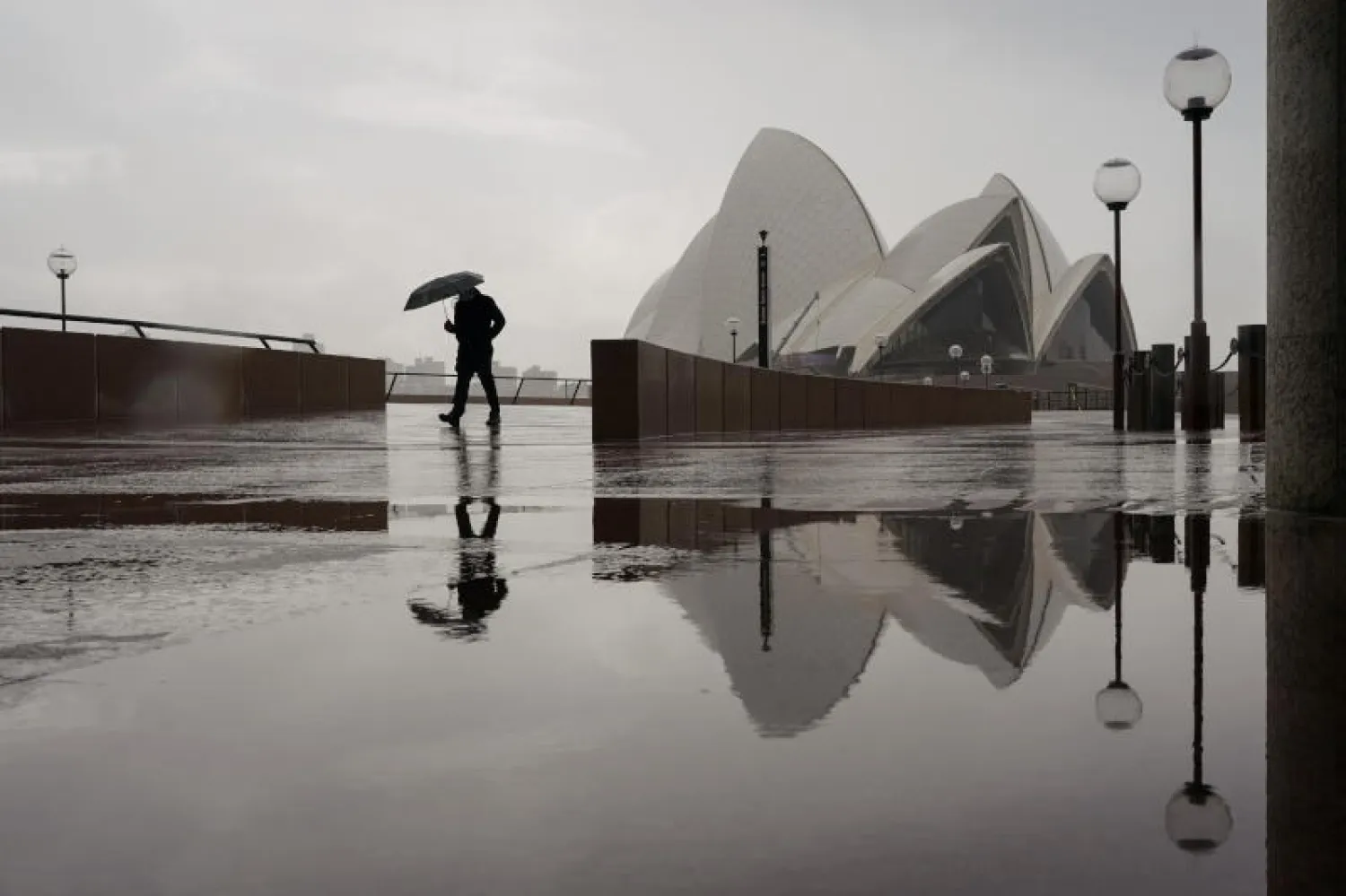 رجل يمشي وحيداً بالقرب من دار الأوبرا في سيدني وسط دخول المدينة في إغلاق لمحاربة تفشي فيروس كورونا (رويترز)