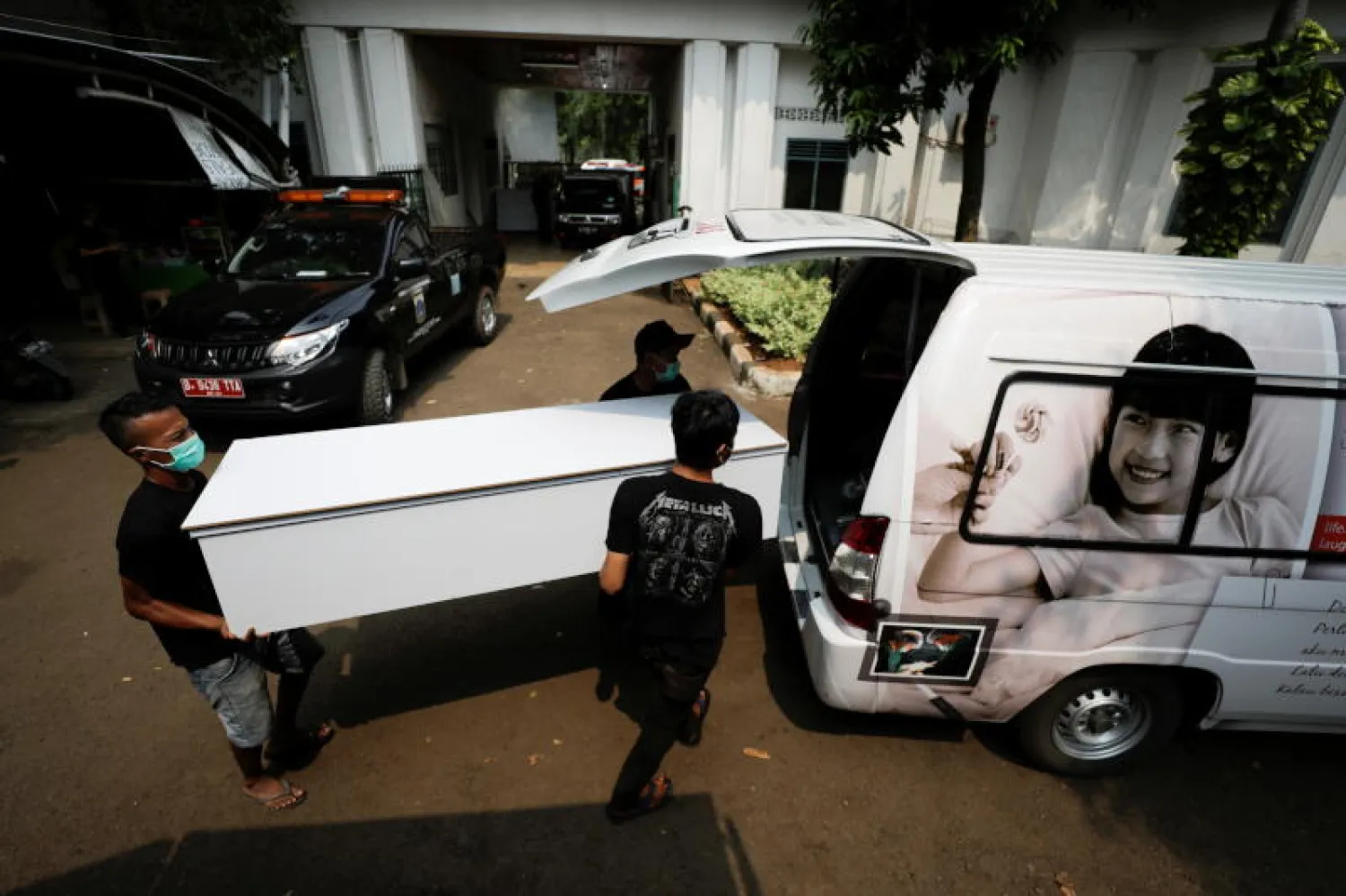 عمال يرتدون أقنعة واقية يقومون بتحميل توابيت فارغة لضحايا مرض فيروس كورونا في سيارة إسعاف لتوزيعها على المستشفى مع زيادة الحالات في جاكرتا (رويترز)