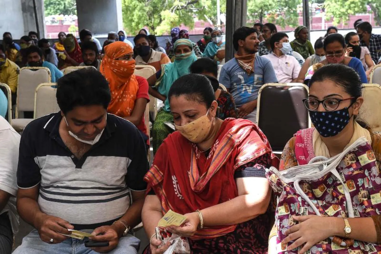 أشخاص ينتظرون دورهم للحصول على لقاح ضد فيروس كورونا بقاعة طاغور في أحمد آباد (أ.ف.ب)