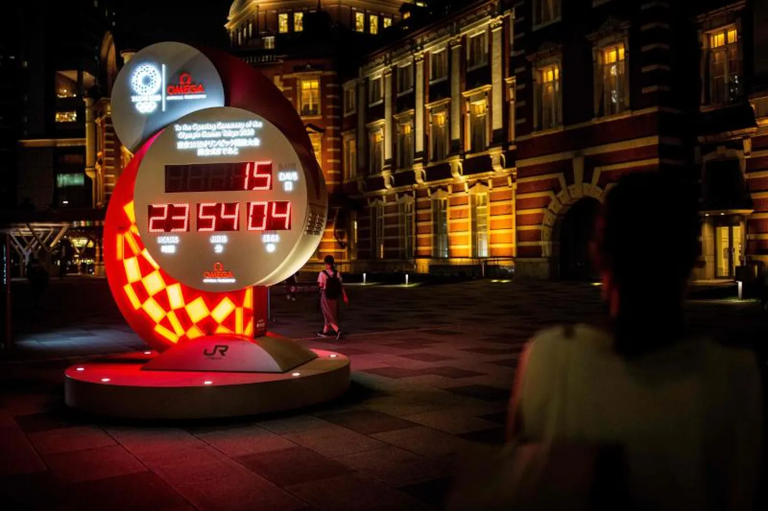 سيدة تنظر إلى ساعة للعد التنازلي لانطلاق أولمبياد طوكيو خارج محطة قطارات في العاصمة اليابانية (أ.ف.ب)