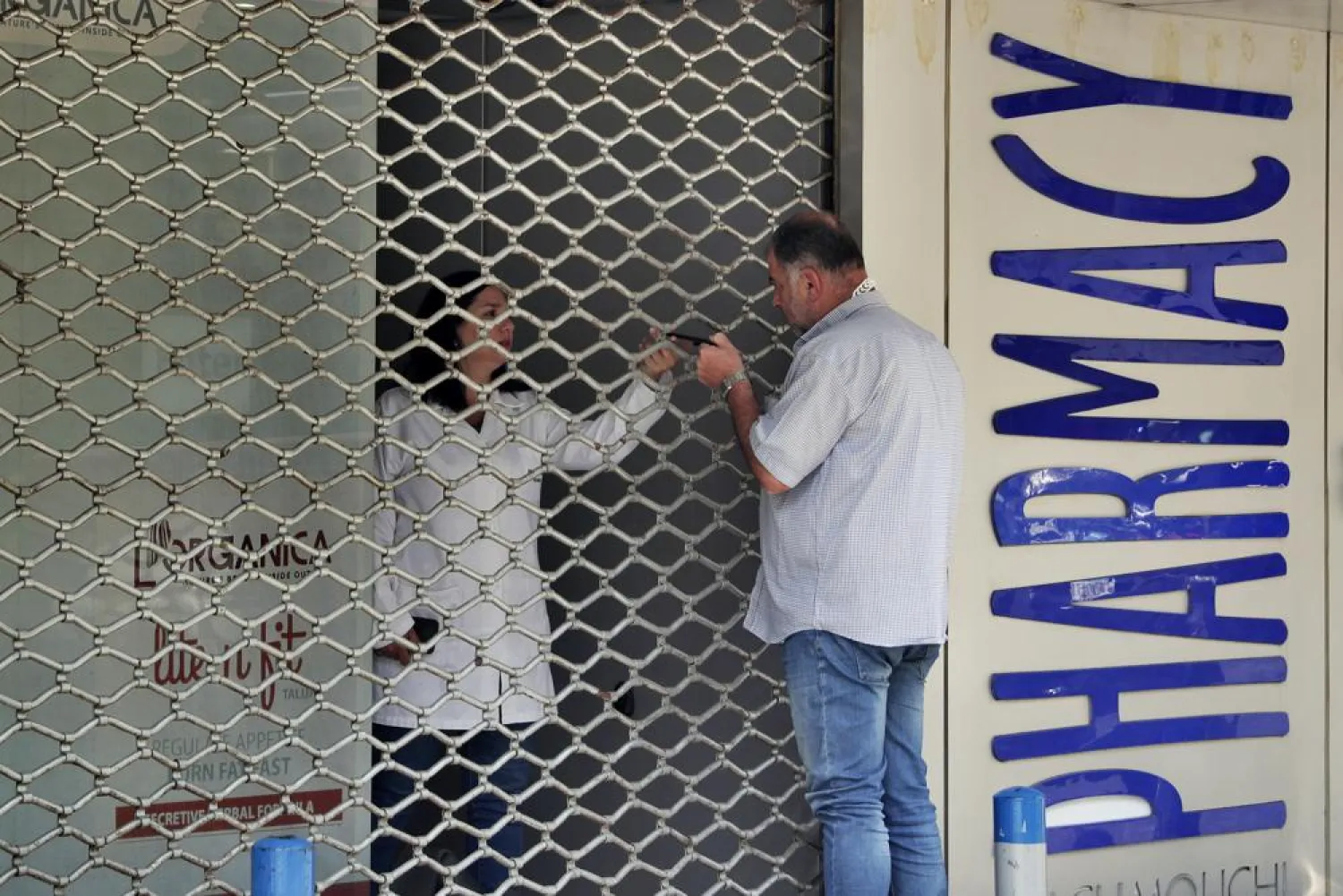 A man speaks with a pharmacist through a closed door of a pharmacy, in Beirut, Lebanon, Friday, June 11, 2021. (AP Photo/Bilal Hussein)